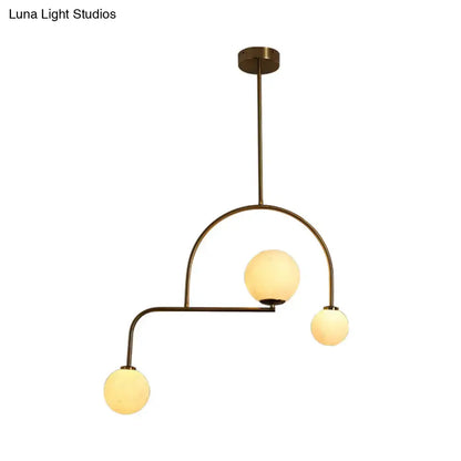 Brass-finished modern global bedroom pendant light with three yellow white frosted glass globe bulbs in an asymmetrical arc
