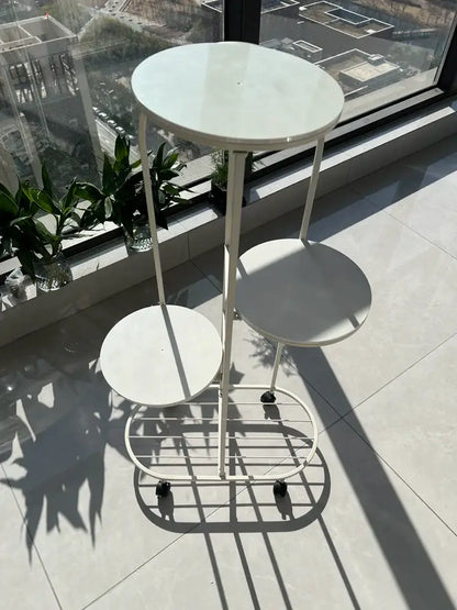 White metal tiered DecorBites™ plant stand with three circular shelves and black caster wheels for interior decor