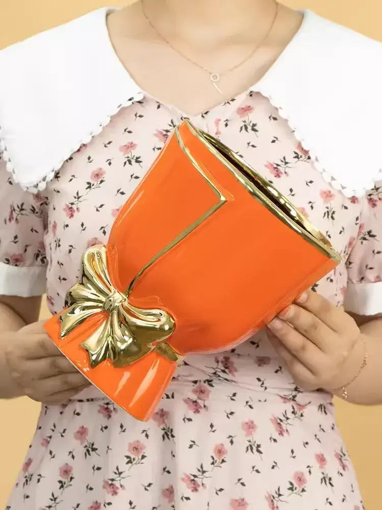 Vibrant orange ceramic vase with glossy finish and gold trim adorned with golden bow for modern nordic home decor