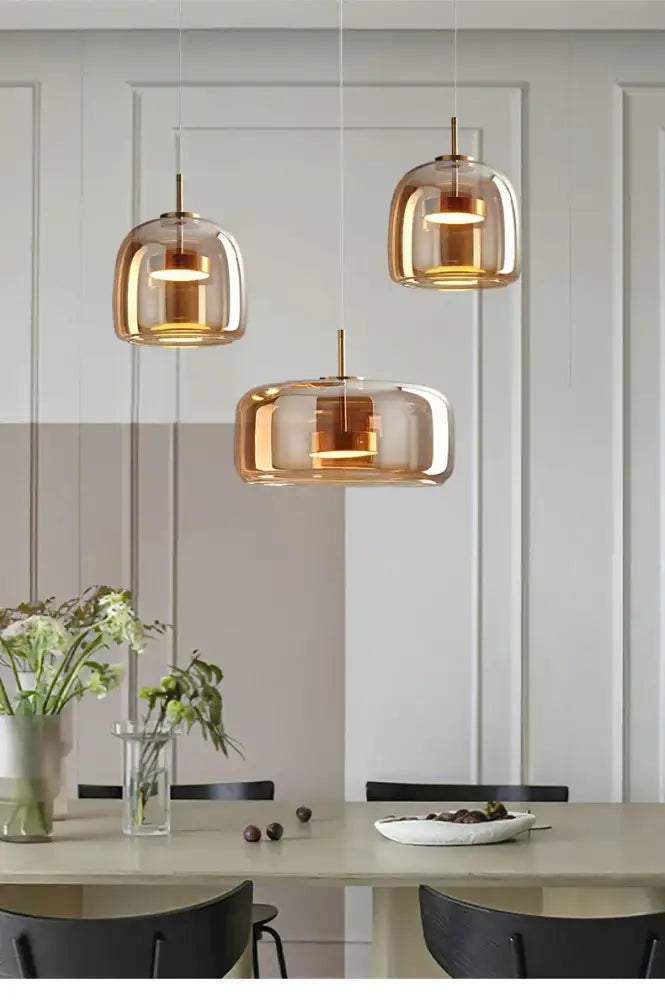 Decorbites modern nordic glass pendant lamp with three amber glass pendant lamps and brass accents above dining table