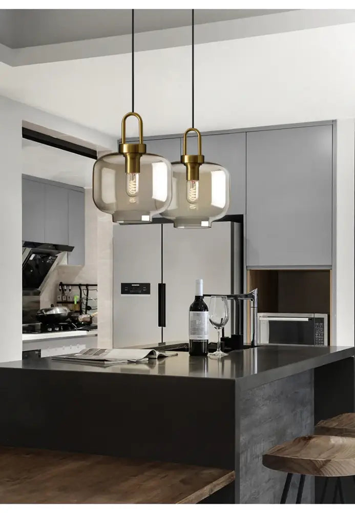 Two elegant brass-finished pendant lights with smoked glass shades hang above a kitchen island decorbites modern glass pendant light