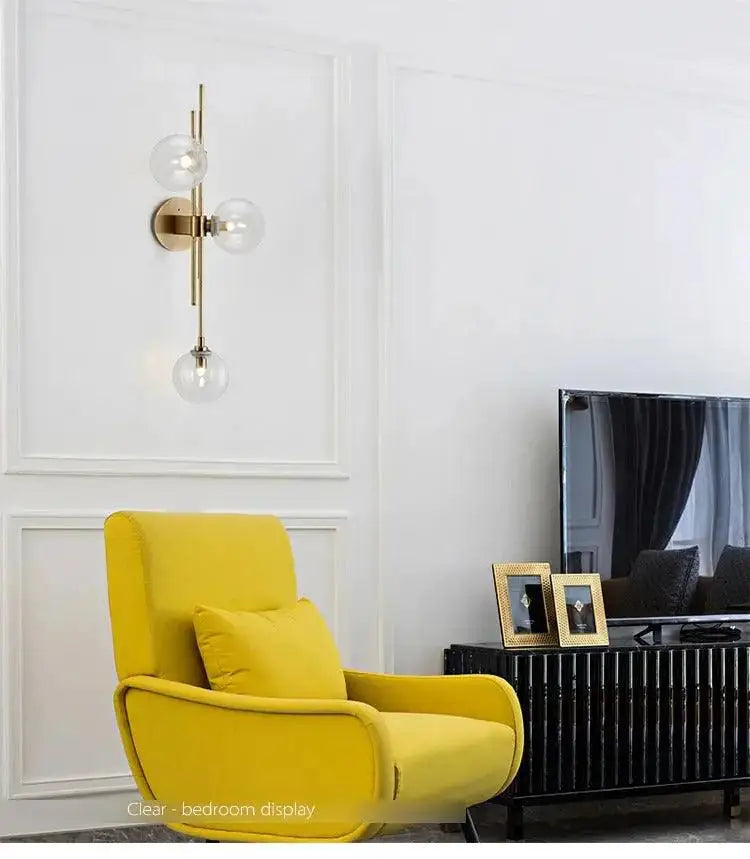 DecorBites modern nordic wall sconce by Adabella features a brass frame with three clear glass globe bulbs vertically arranged