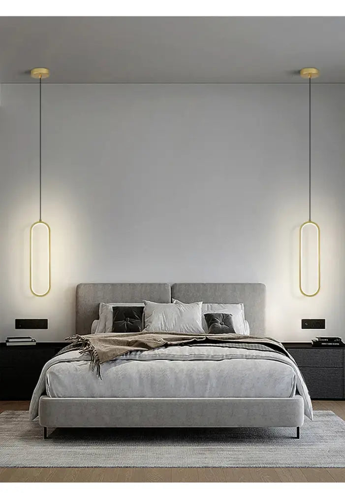Modern gold-toned nordic pendant lights hang symmetrically above a gray upholstered bed in a DecorBites™ pendant light setup
