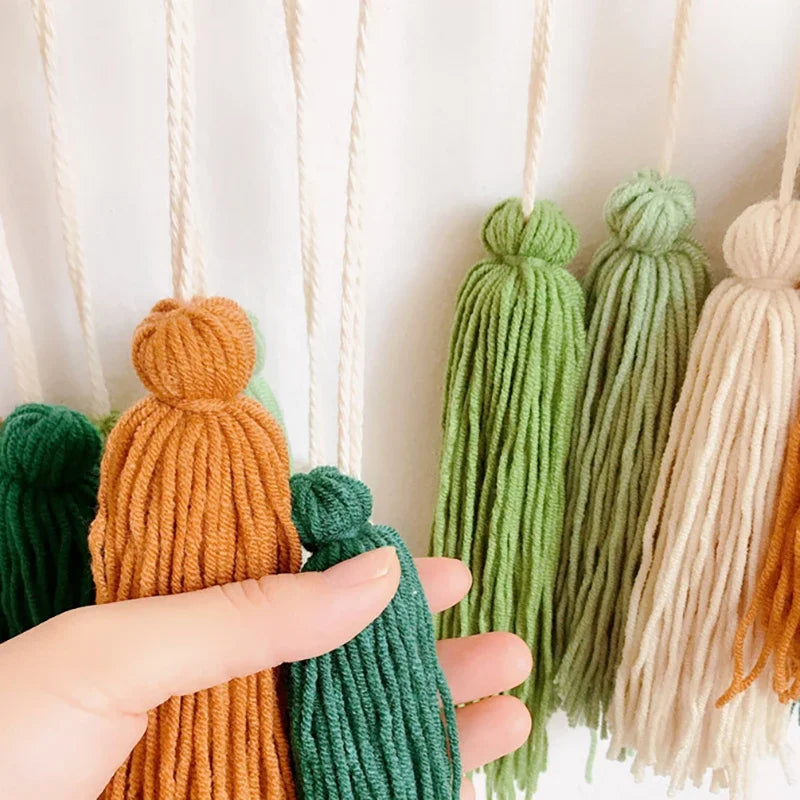 A hand holds colorful textured yarn tassels in earthy tones for a moroccan bohemian wall decor tapestry
