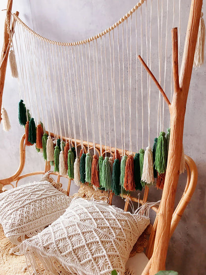 Decorbites moroccan bohemian wall decor macramé tassel garland with wooden beads in green orange white and brown above rattan bench
