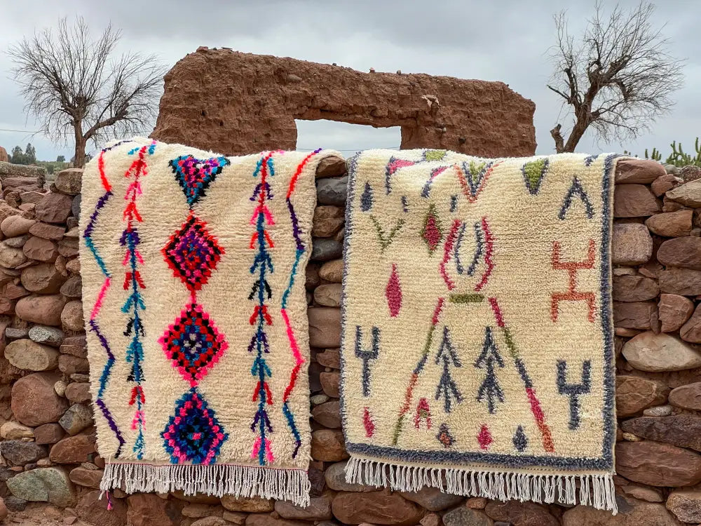 Two moroccan handmade azilal rugs with vibrant pink blue purple and green geometric patterns on cream background