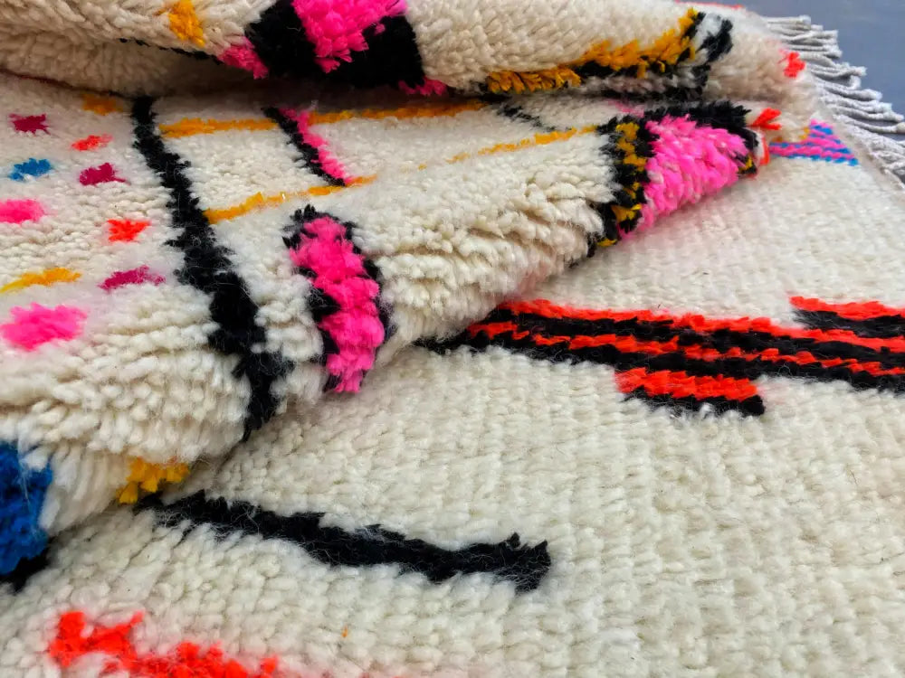 A plush cream-colored decorbites moroccan handmade azilal rug with vibrant pink black orange and red geometric patterns