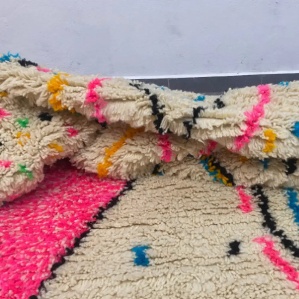 A cream-colored decorbites moroccan handmade azilal rug with vibrant pink black yellow and blue geometric patterns