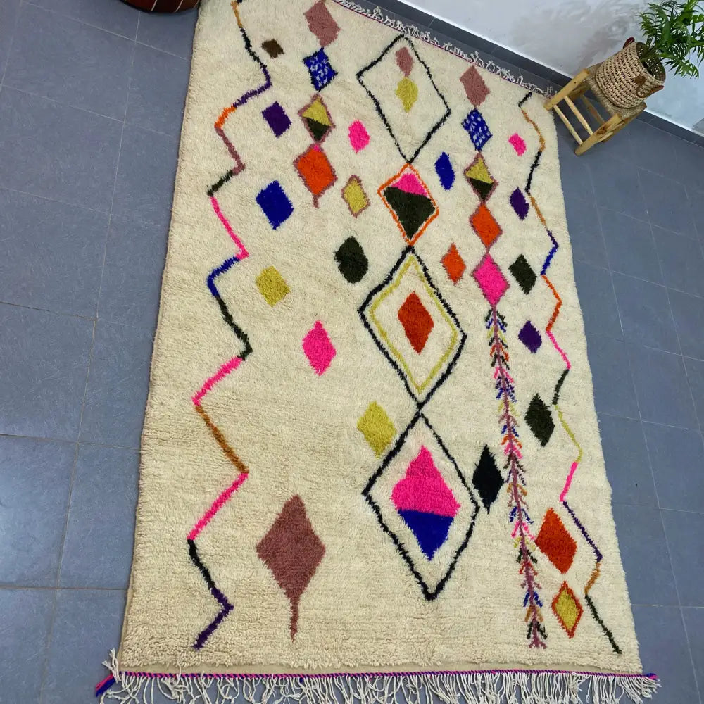 Cream-colored moroccan handmade azilal rug with vibrant pink blue orange and green geometric patterns on fluffy wool base