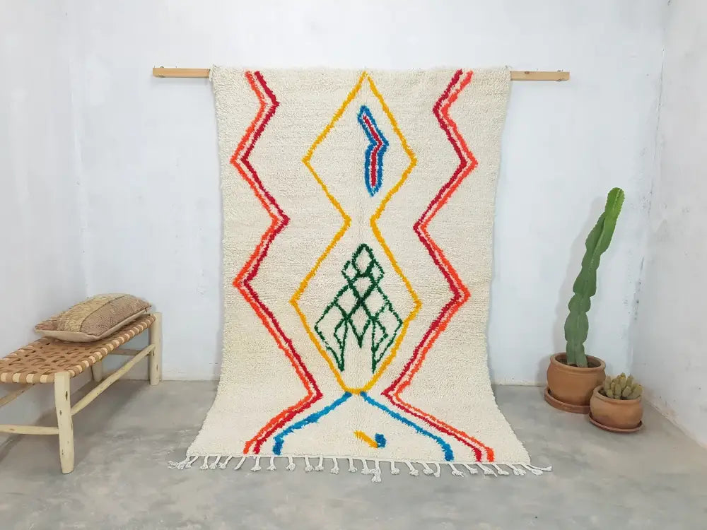 Cream-colored moroccan handmade azilal berber carpet with bold red yellow and blue geometric patterns on woolen surface