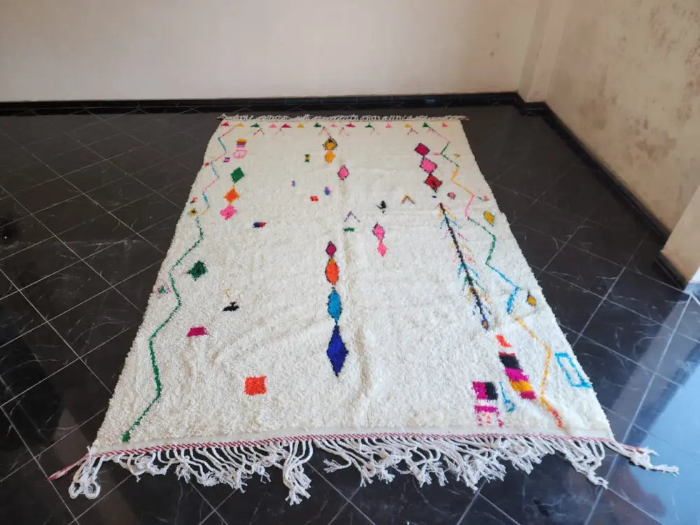 A vibrant off-white moroccan handmade azilal berber carpet with colorful geometric patterns and long white fringe supporting sustainable practices