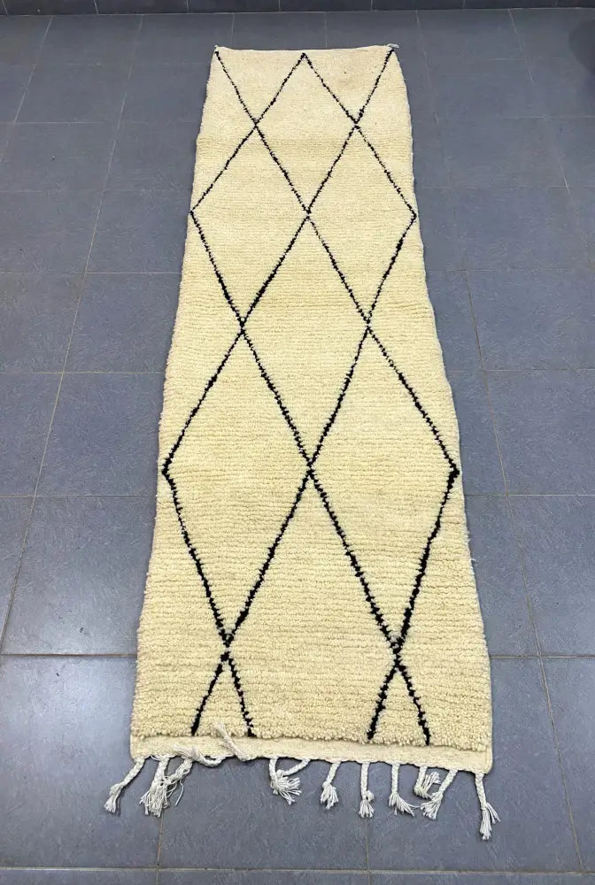 Cream-colored moroccan handmade beni ouarain rug with black geometric diamond patterns and white fringe 2.8m x 0.7m