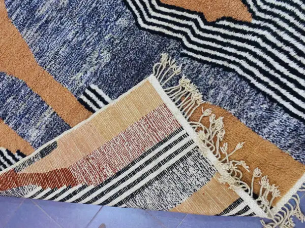 A moroccan handmade beni ouarain rug featuring bold navy blue orange black and white geometric patterns with fringed edge