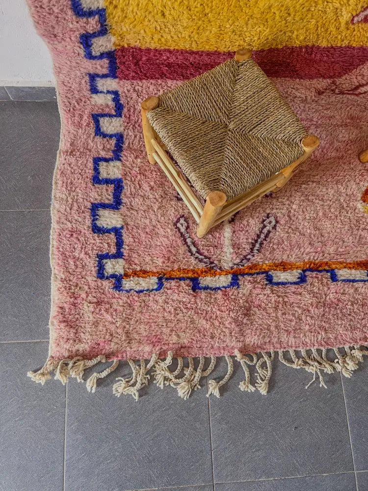 A woven wicker stool with wooden legs in natural light brown next to a moroccan handmade beni ouarain rug 3m x 2.5m