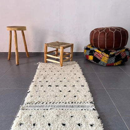 A cream-colored textured wool moroccan handmade beni ouarain rug with black dot patterns and fringed edge