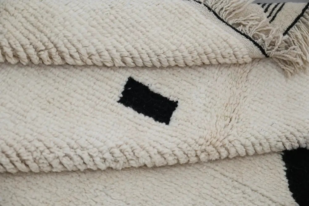 Cream-colored thickly woven moroccan handmade traditional azilal rug with black geometric patterns and fringed edges