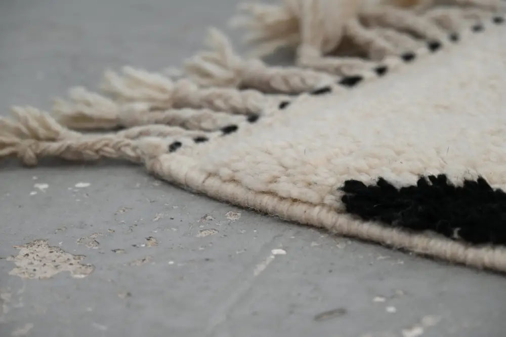 Cream-colored wool moroccan handmade traditional azilal rug with black fringe and stitched border details 224 x 152 cm