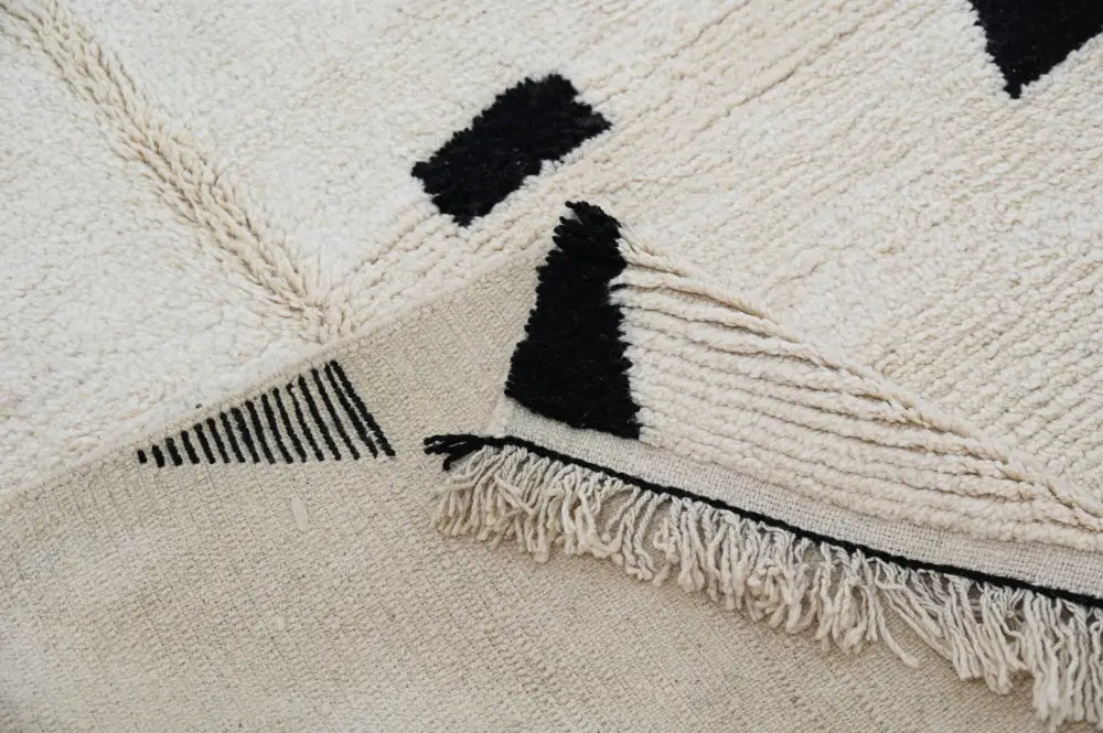 Cream-colored moroccan handmade traditional azilal rug with black geometric patterns and fringed edges by DecorBites