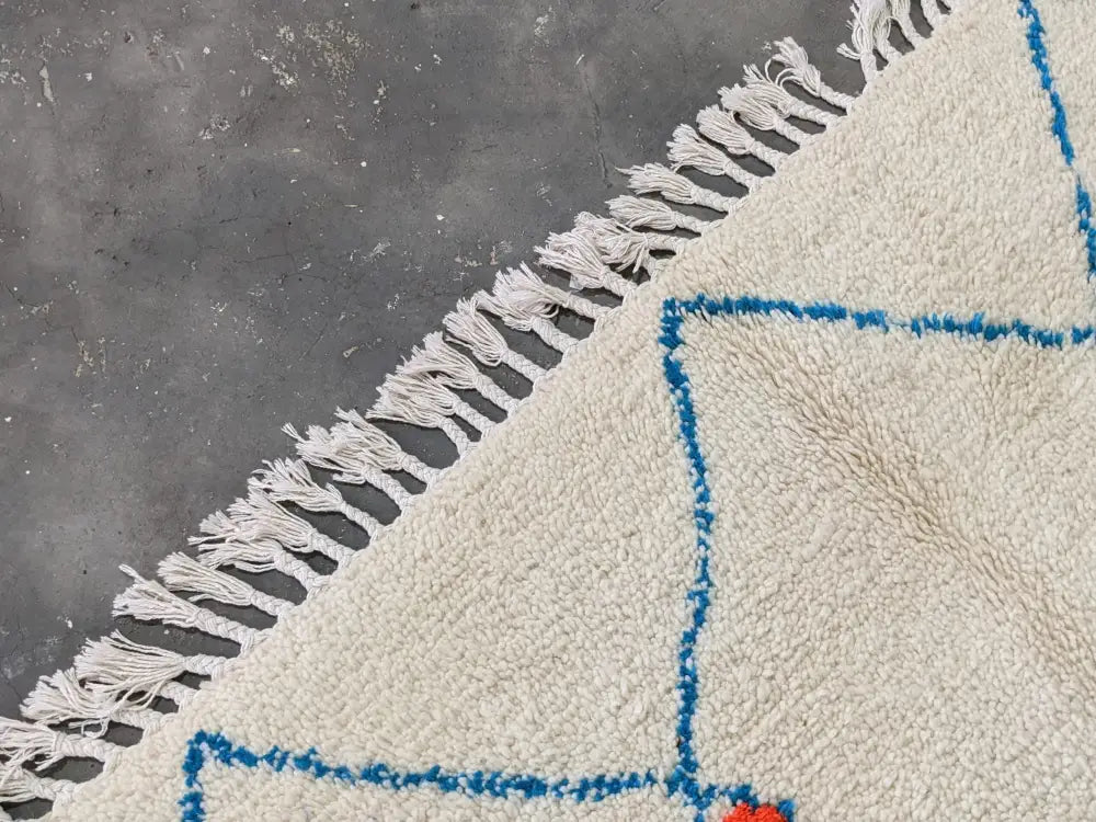 Cream-colored moroccan handmade azilal rug with blue geometric patterns and white fringe made of pure natural wool