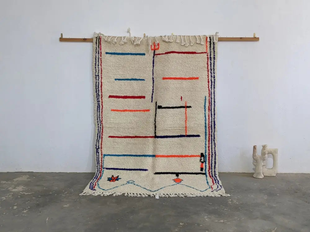 A cream-colored moroccan handmade azilal rug with bold red blue and black geometric patterns in pure natural wool