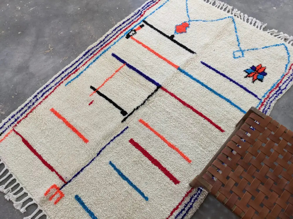 Cream-colored moroccan handmade azilal rug with bold geometric patterns in red blue black orange made of pure natural wool