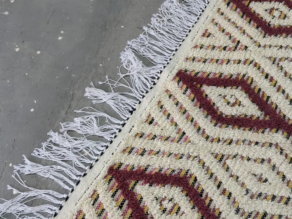 Cream-colored DecorBites moroccan handmade traditional azilal rug with maroon geometric patterns and thick white fringe