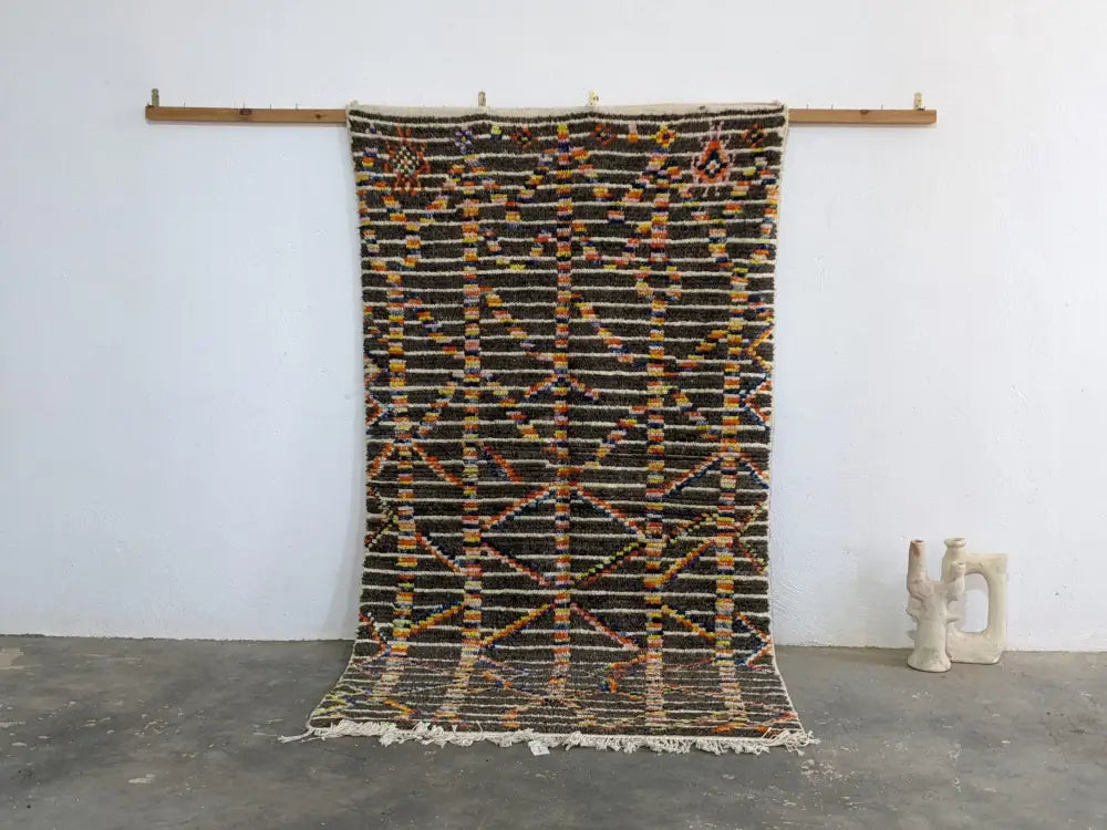 A moroccan handmade azilal rug by decorbites with dark brown base geometric patterns in orange yellow black pure natural wool