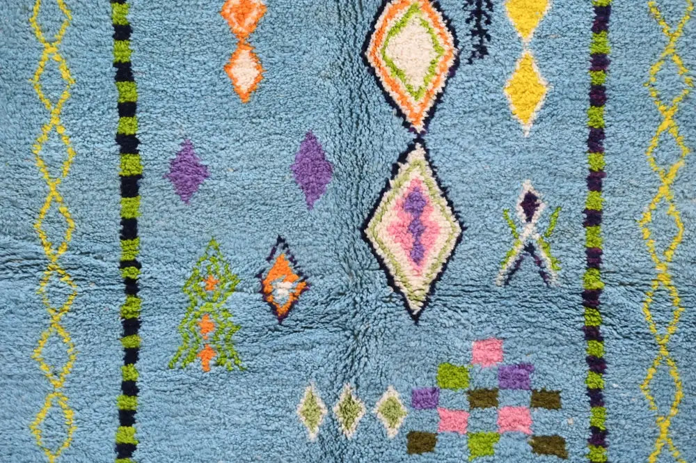 A plush light blue moroccan handmade traditional azilal rug with vibrant orange purple green and pink geometric patterns
