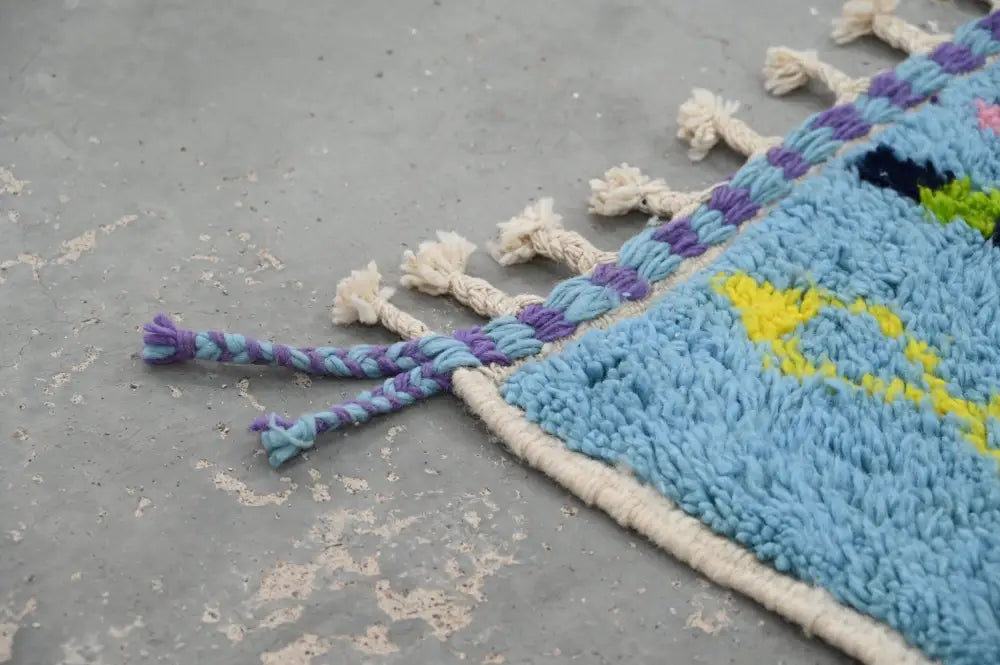Blue and purple braided tassels adorn the edge of a cream bordered moroccan handmade traditional azilal rug by decorbites