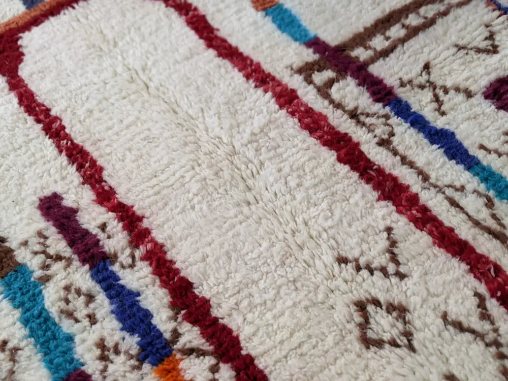 A plush white moroccan handmade traditional azilal rug with bold red blue and brown geometric patterns in thick wool