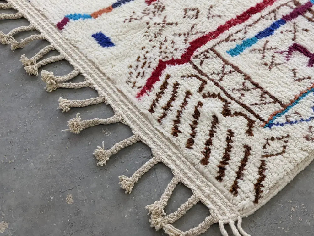 Cream-colored moroccan handmade traditional azilal rug with intricate red blue brown wool patterns and fringed edge 250 x 150 cm