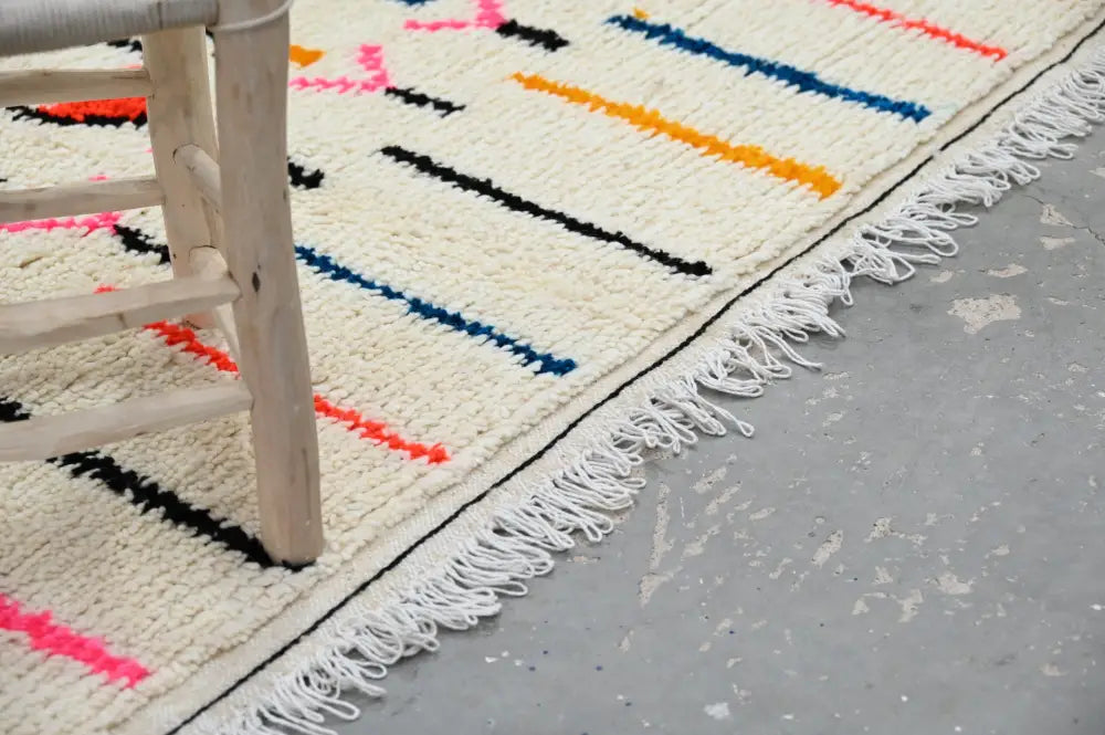 Cream-colored moroccan handmade traditional azilal rug with bold black blue orange and pink geometric stripes and white fringe
