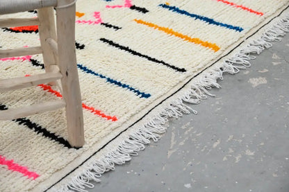 Cream-colored moroccan handmade traditional azilal rug with bold black blue orange and pink geometric stripes and white fringe