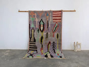 A vibrant moroccan handmade azilal rug in pure natural wool with textured weave and fringe hanging on wooden rod