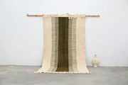 Beige and olive green moroccan handmade traditional azilal rug with woven texture and frayed edges hanging on wooden rod