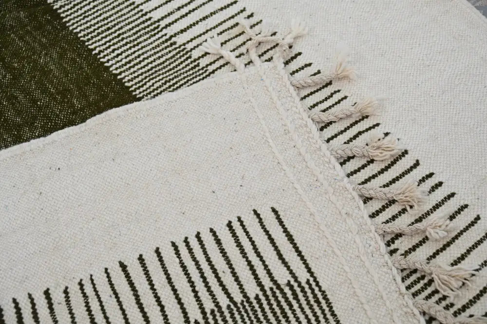 A cream-colored moroccan handmade traditional azilal rug with black geometric stripes and fringed edges by decorbites