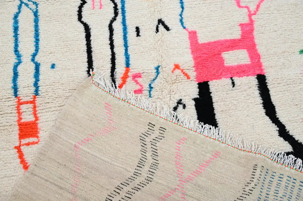 A cream-colored moroccan handmade traditional azilal rug with bold black pink blue and orange geometric patterns by decorbites
