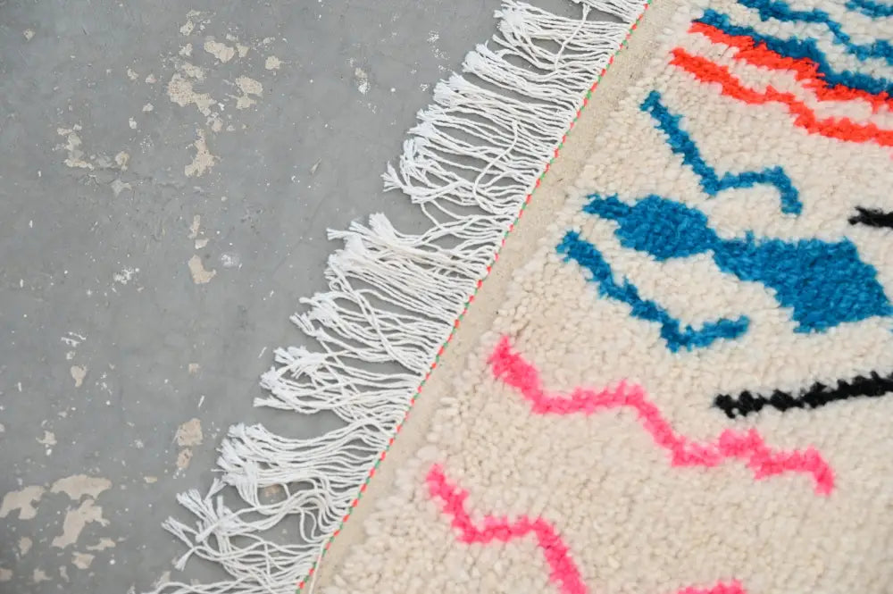 Cream-colored moroccan handmade traditional azilal rug with bold blue pink black geometric patterns and white fringe