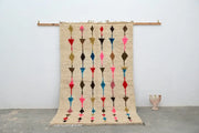 Beige woven moroccan handmade traditional azilal rug with vertical rows of colorful geometric shapes in pink red blue and brown
