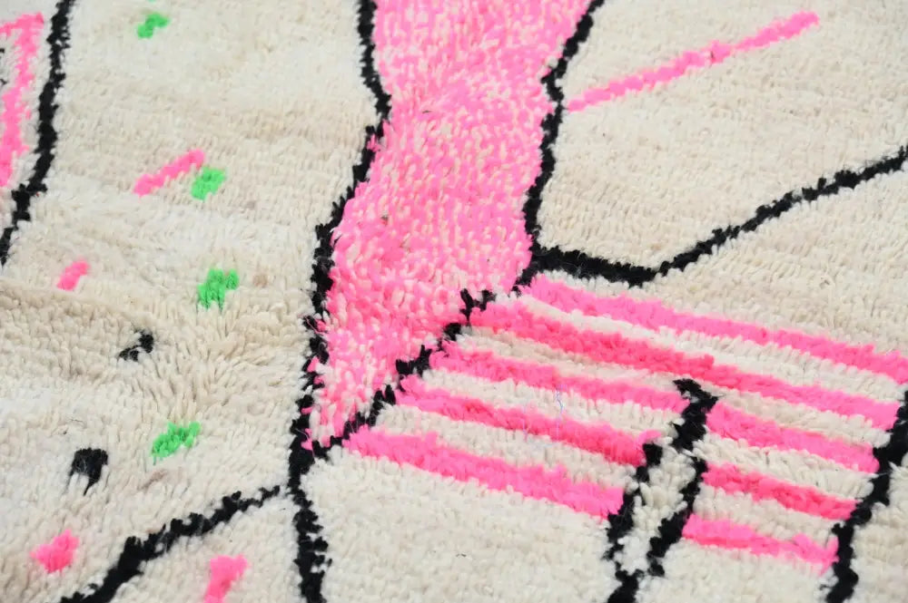 A cream moroccan handmade traditional azilal rug featuring bold pink and black geometric patterns with green accents