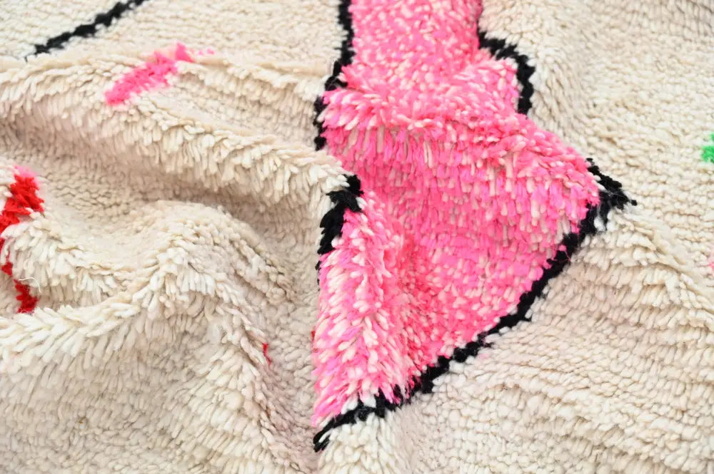 A plush cream-colored moroccan handmade traditional azilal rug with vibrant pink and black geometric patterns in textured fluffy material
