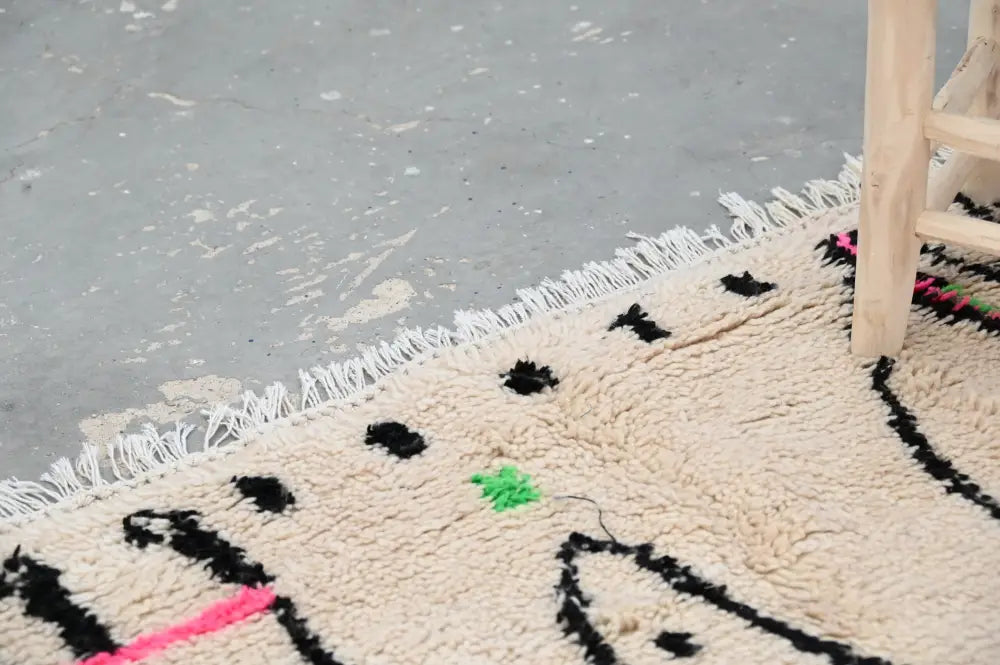 Cream-colored moroccan handmade traditional azilal rug with black and pink geometric patterns and white fringe by decorbites