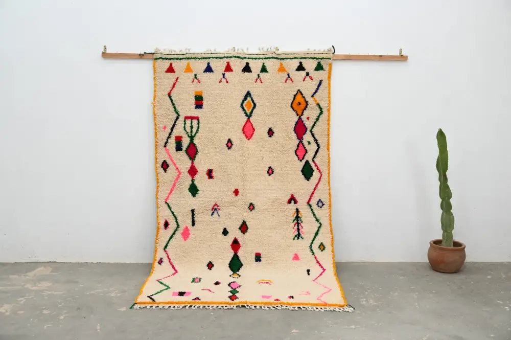 Beige moroccan handmade traditional azilal rug with vibrant pink green orange and red geometric patterns on woolen surface