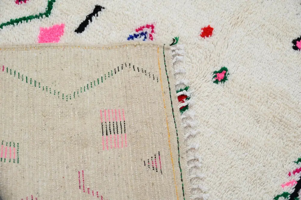 Cream-colored moroccan handmade traditional azilal rug with fluffy texture and geometric pink green black and red patterns