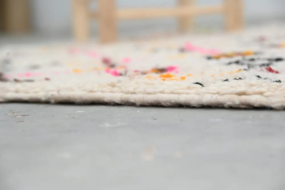 A cream-colored moroccan handmade traditional azilal rug with vibrant pink orange and black accents along textured edge