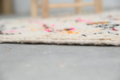 A cream-colored moroccan handmade traditional azilal rug with vibrant pink orange and black accents along textured edge