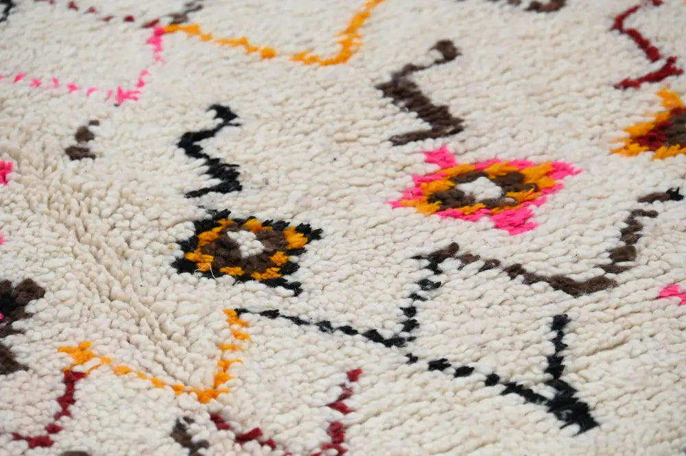 A cream-colored moroccan handmade traditional azilal rug with vibrant pink orange black and brown geometric patterns