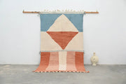 Moroccan handmade traditional azilal rug in soft blue terracotta and cream tones with fringed edges hanging on wooden rod
