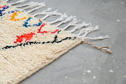 Cream-colored moroccan handmade traditional azilal rug with vibrant red blue yellow patterns and long white fringe by DecorBites