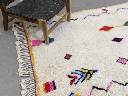 A vibrant cream-colored moroccan handmade traditional azilal rug with colorful geometric patterns and fringed edges